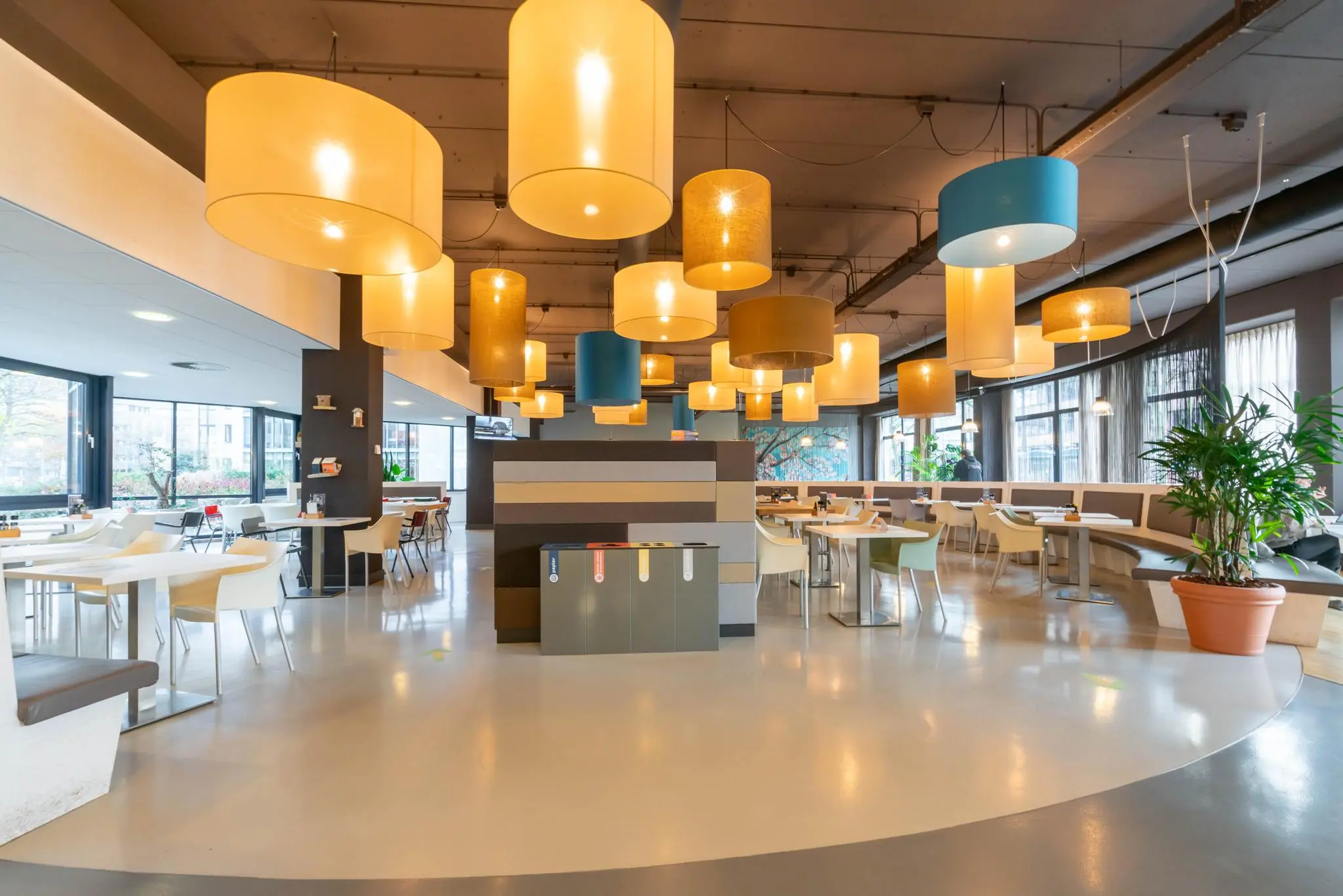 Modern ingerichte kantine aan de De Bruyn Kopsstraat met kleurrijke hanglampen en een centraal afvalscheidingsstation.